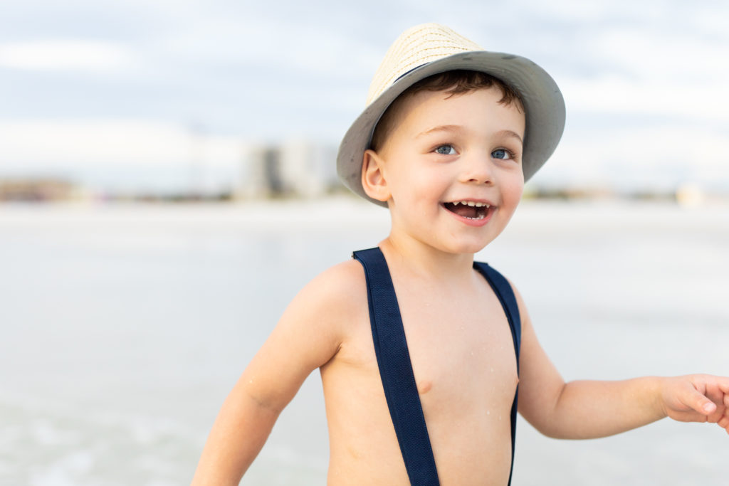 boy at the beach in hat and suspenders