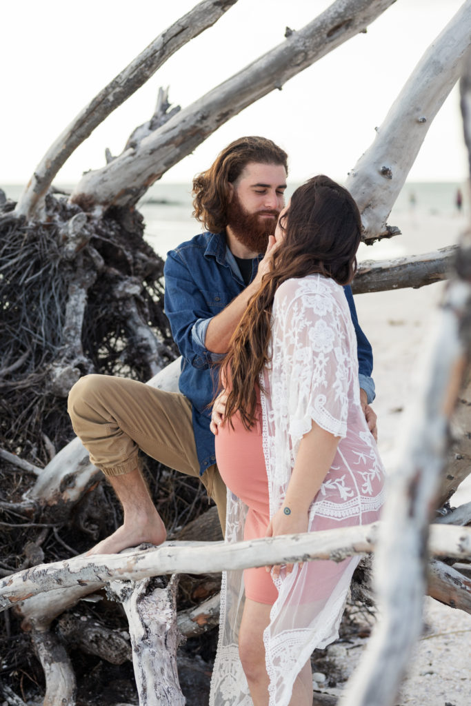 man and pregnant wife in driftwood at the beach