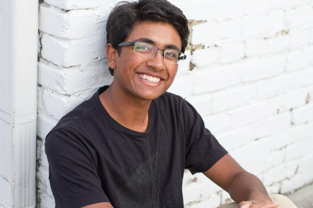 boy sitting against white brick wall