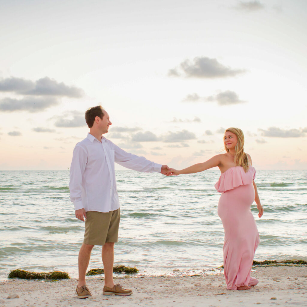 pregnant woman walking on beach holding husband's hand