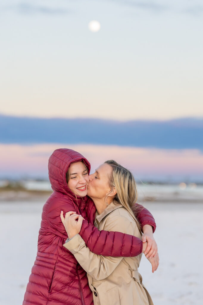 mom kissing teen daughter's cheek at the beach