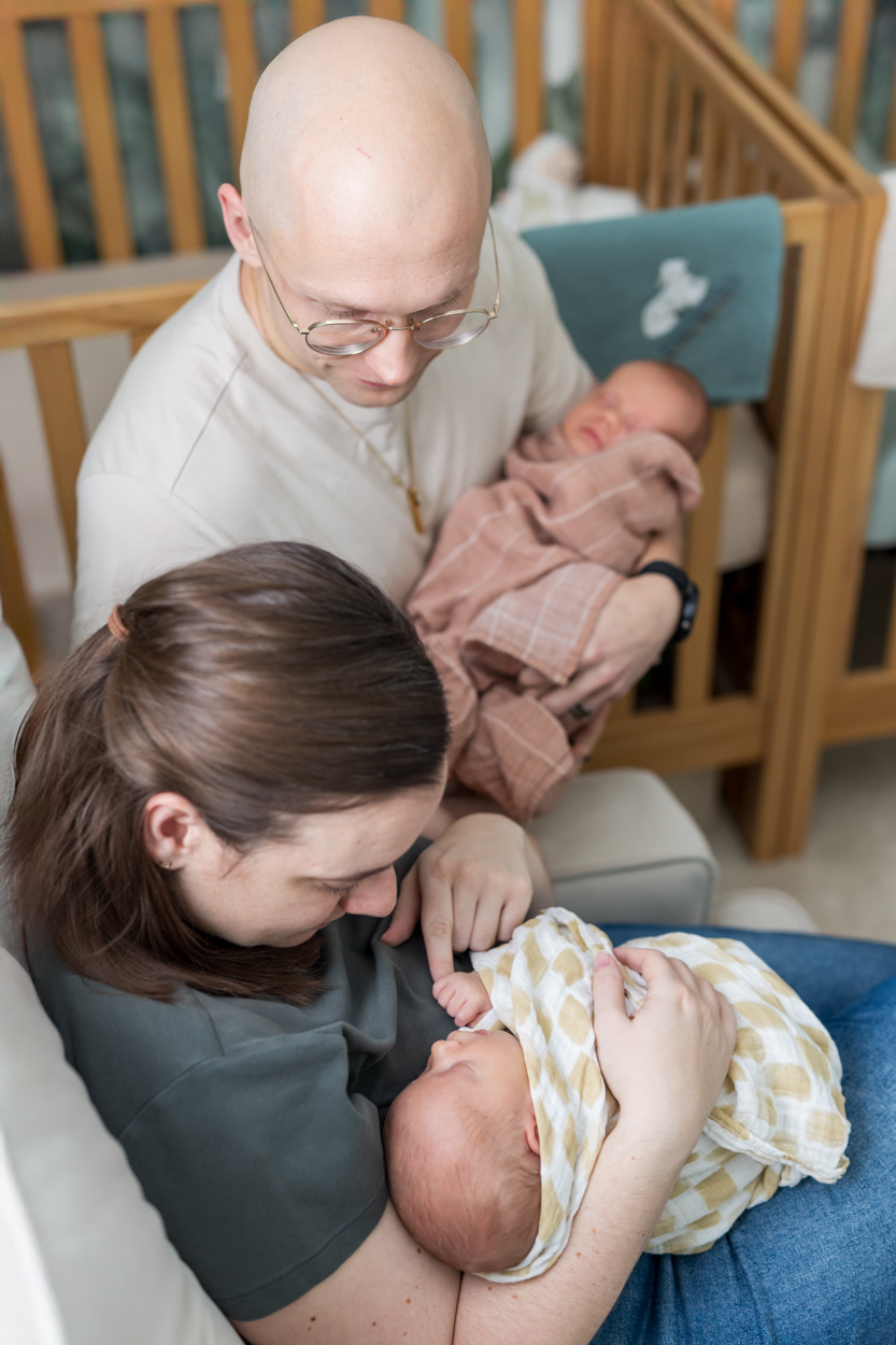new mom holding babies finger, while dad and twin baby look on