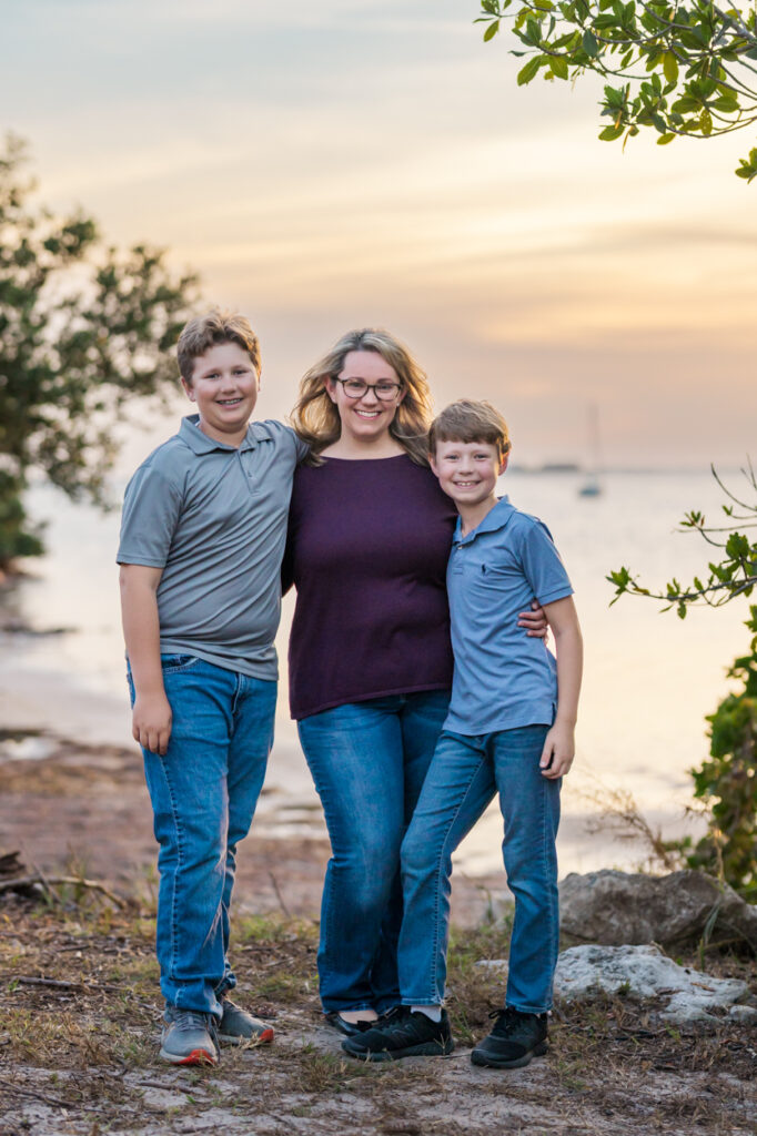 mom smiling at the camera with two boys, beach sunset behind them