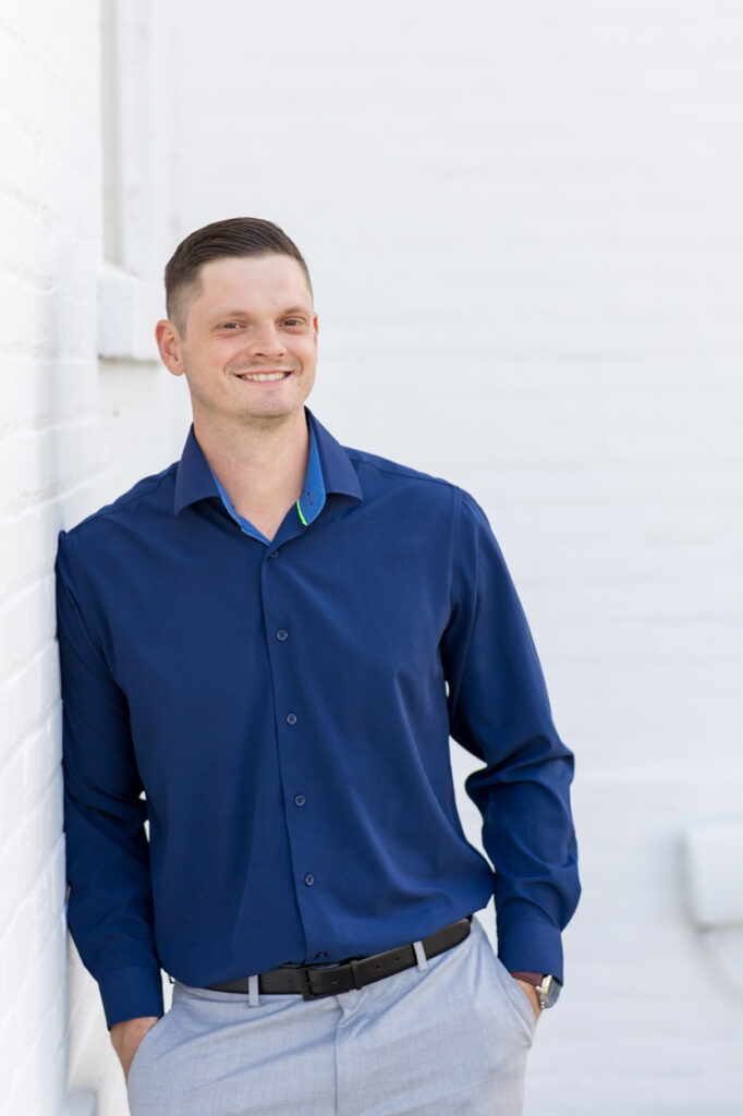man in blue shirt leaning on white wall for headshots