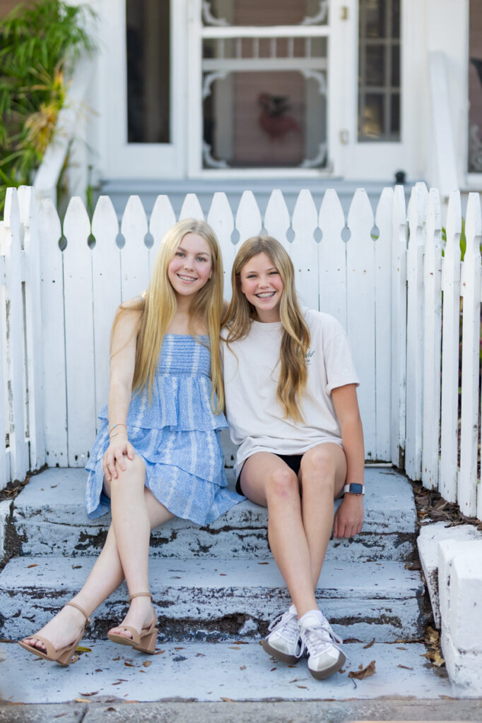 two girls sitting on steps with white picket fence