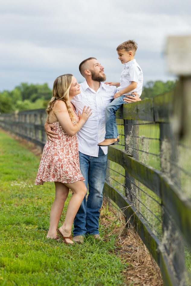 mom and dad sitting her boy up on a fence