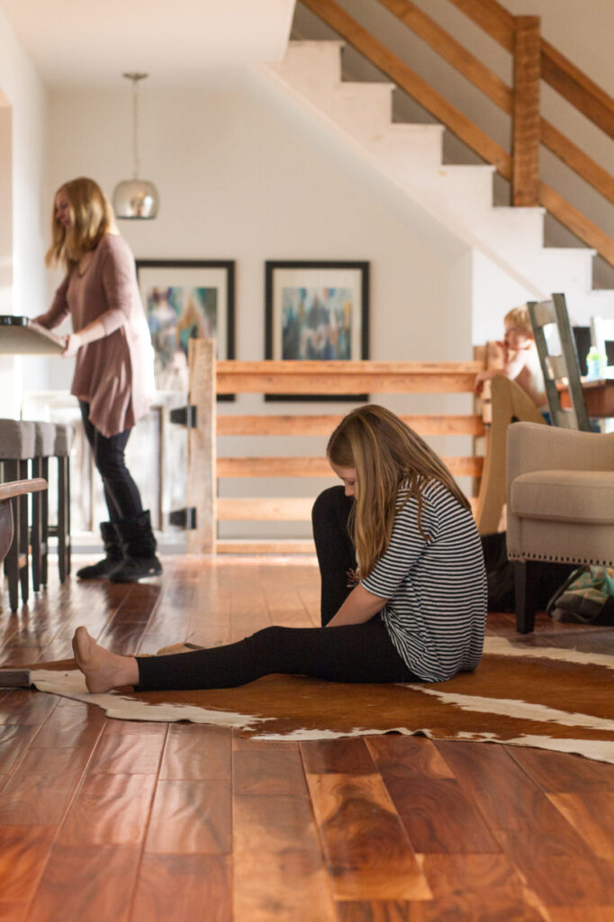 girl putting on ballet shoes while mom cleans